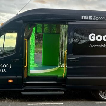 The goodysphere sensory bus parked, at dusk, with the door open revealing the green bubble tube, padded flooring and cascading fibre optic waterfall