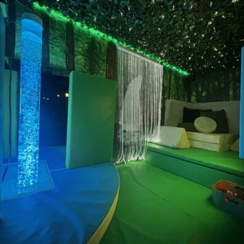 the interior of the mobile sensory unit with bubble tube glowing aqua, and the shining fibre optics. There is a sofa at the back with cushions on it.