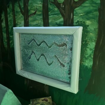 a sequin board is mounted on a rainforest mural. there are two squiggly lines drawn in the sequins.
