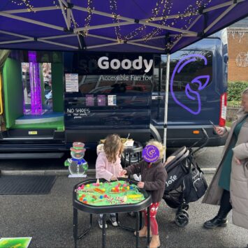 two women and young children stand engaging with the sensory trays outside the Goodysphere Mobile sensory bus.