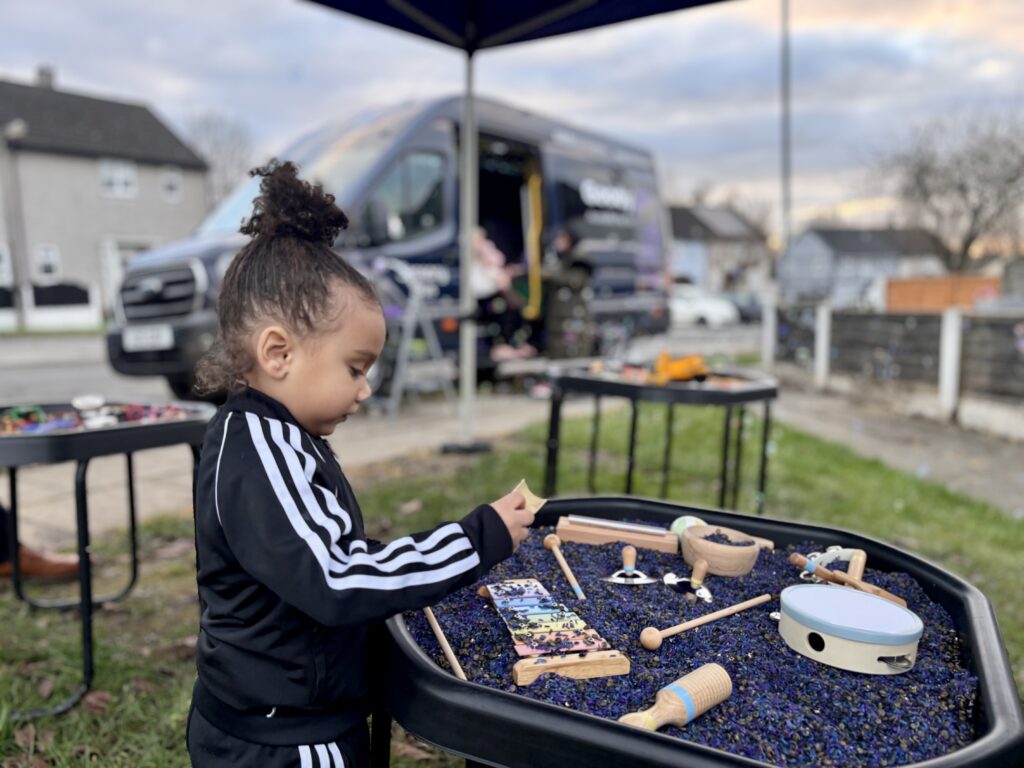 A young boy plays with a music themed sensory tray, the goodysphere sensory bus is blurred in the background creatively.