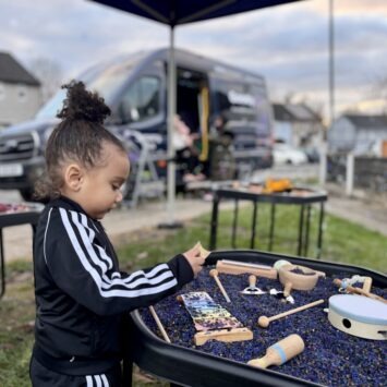 A young boy plays with a music themed sensory tray, the goodysphere sensory bus is blurred in the background creatively.