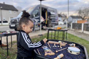 A young boy plays with a music themed sensory tray, the goodysphere sensory bus is blurred in the background creatively.