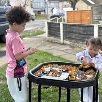 a young boy and toddler girl play with a sensory tray containing diggers.