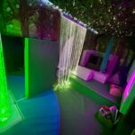 the interior of the mobile sensory unit with bubble tube glowing green, and the shining fibre optics. There is a sofa at the back with cushions on it.