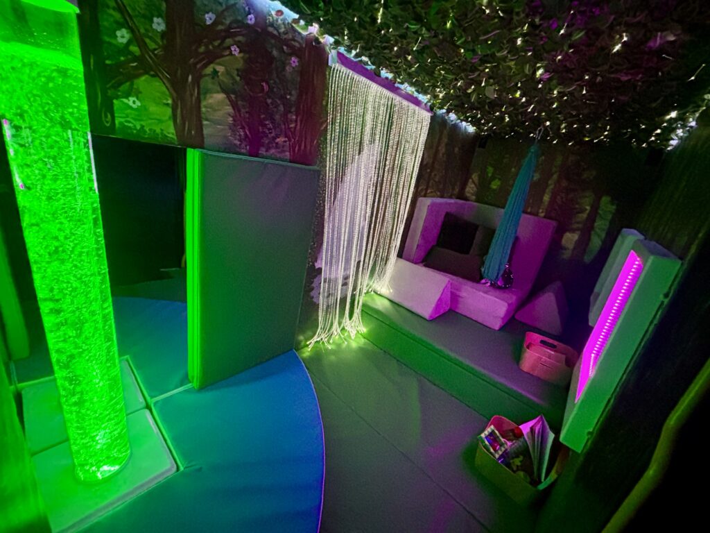 the interior of the mobile sensory unit with bubble tube glowing green, and the shining fibre optics. There is a sofa at the back with cushions on it.
