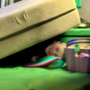 Mostly hidden, a young boy receives deep pressure stimulation under the large sofa cushions.