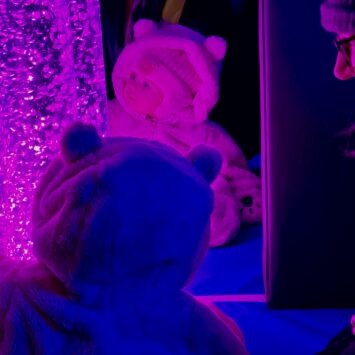 An adorable baby wearing a bear outfit stares at the purple bubbles