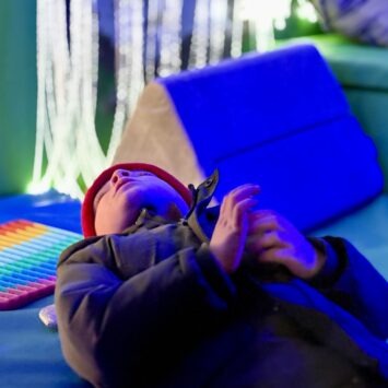 a young boy lays down looking up at the bubble tube, toys are scattered around him and the fibre optic curtain is blurred creatively behind him.