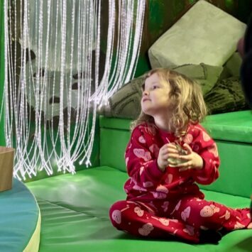 a young girl in red squashes a fidget toy as she sits with the drapes fibre optics behind her.