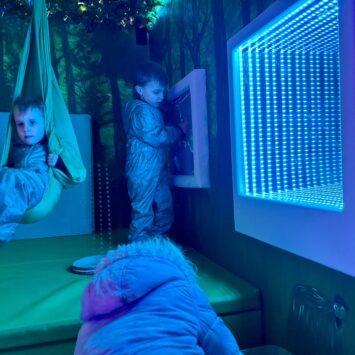one child sits in the swing whilst another plays with the sequin board on the goodysphere sensory bus