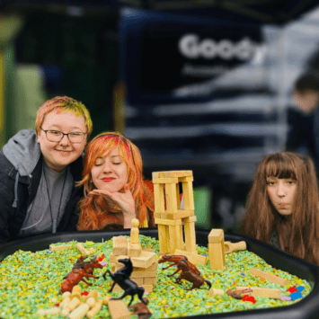 Three teenagers smile proudly behind their masterpiece of a tower on a sensory tray.