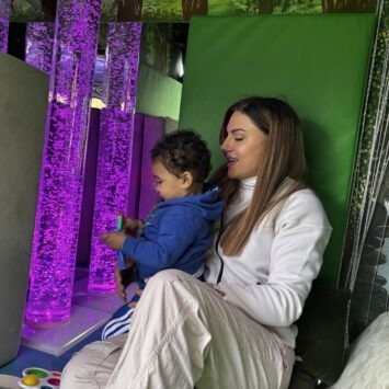 A mother and son sit together looking at the purple bubble tube inside the goodysphere sensory bus