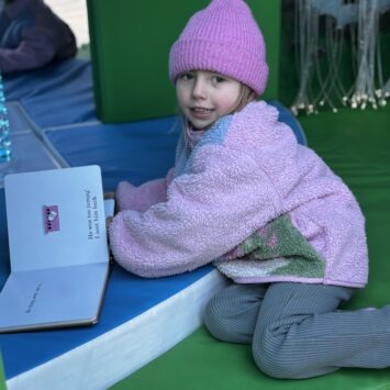 a young girl in a hat kneels whilst reading a book