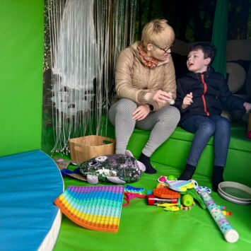 A lady sits with a young boy playing with sensory toys together inside the Goodysphere Sensory Bus
