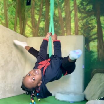 girl displays gymnastic skills on sensory swing hanging upside down